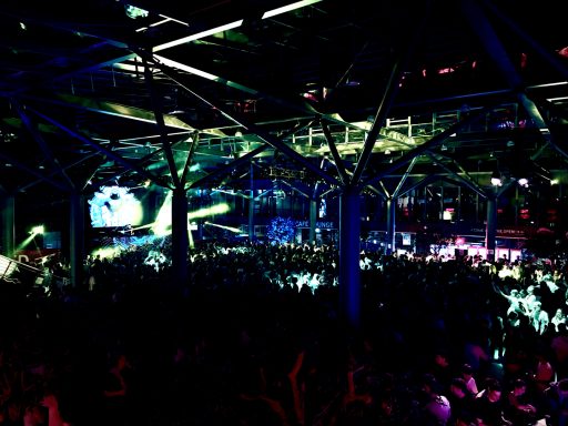 Große Menschenmenge in einer beleuchteten Veranstaltungshalle mit bunten Lichtern.