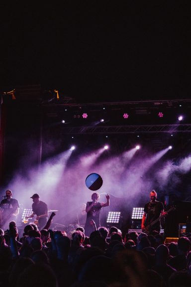 Ein Konzert mit Band auf Bühne, bunte Lichter und Menschenmenge, die einen Ball werfen.